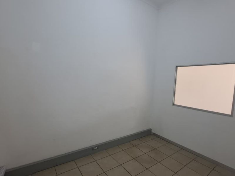 A clean, empty office space featuring neutral tiled flooring and an internal window, suitable for a professional workspace or administrative area.