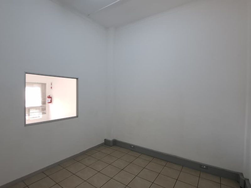A clean, empty office space featuring neutral tiled flooring and an internal window looking into an adjacent area.