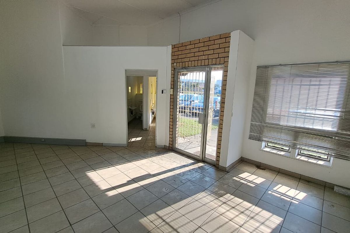 An open-plan entry area featuring tiled flooring, a brick accent wall, and a secure metal entrance gate with access to an adjacent restroom.
