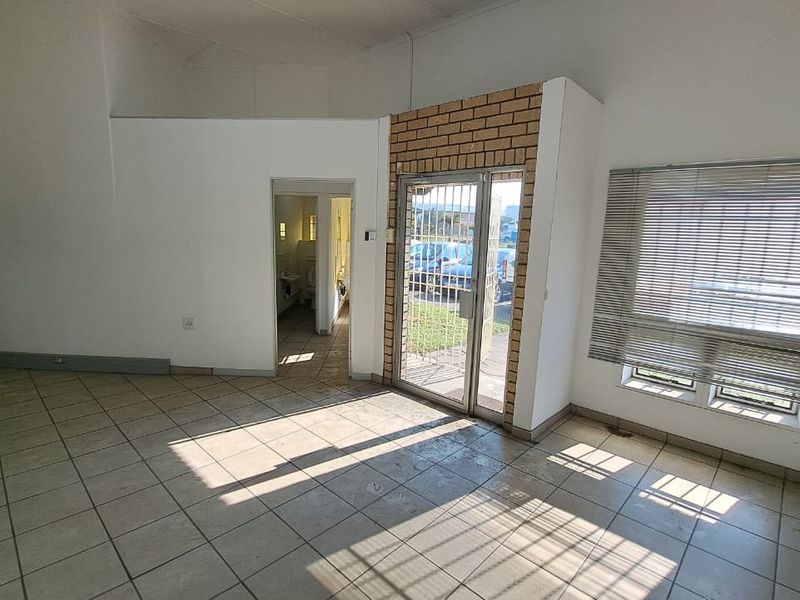 An open-plan entry area featuring tiled flooring, a brick accent wall, and a secure metal entrance gate with access to an adjacent restroom.