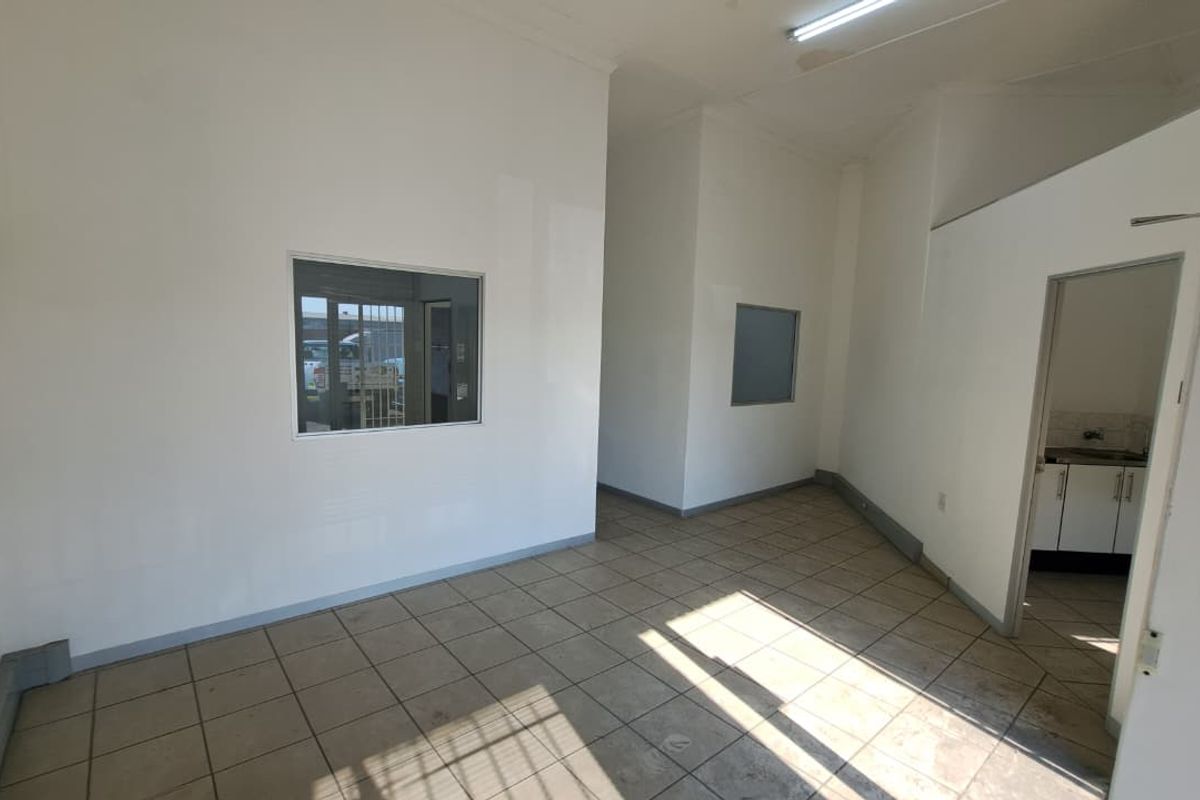 An empty industrial office space featuring tiled flooring, internal windows, and neutral walls, providing a functional and versatile workspace.