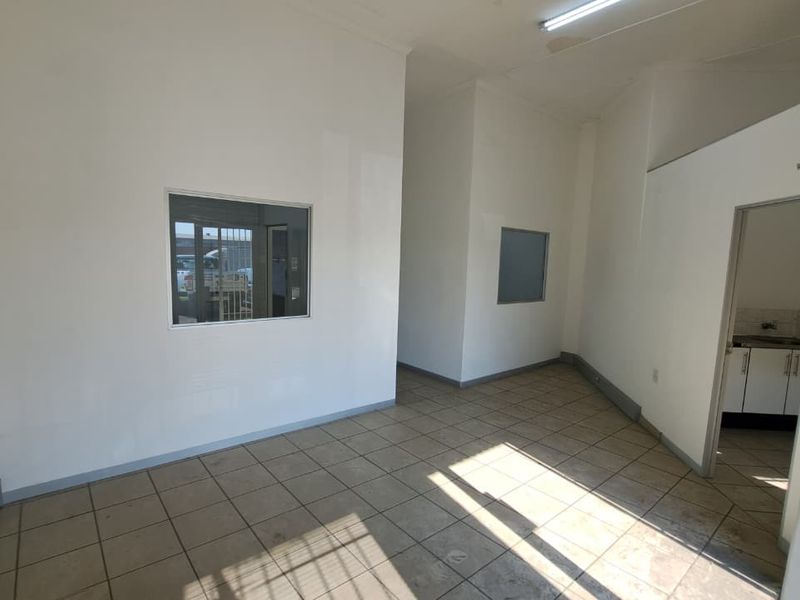An empty industrial office space featuring tiled flooring, internal windows, and neutral walls, providing a functional and versatile workspace.