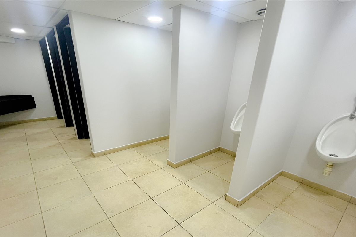 A functional commercial restroom featuring tiled flooring, wall-mounted urinals with privacy partitions, and recessed ceiling lighting.