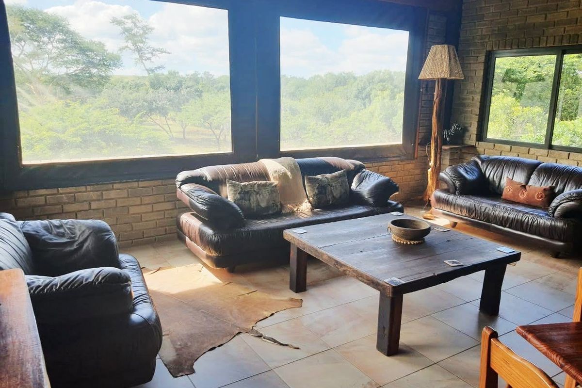 Spacious living area featuring exposed brick walls, large windows with scenic landscape views, and tiled flooring, offering a rustic and comfortable atmosphere.