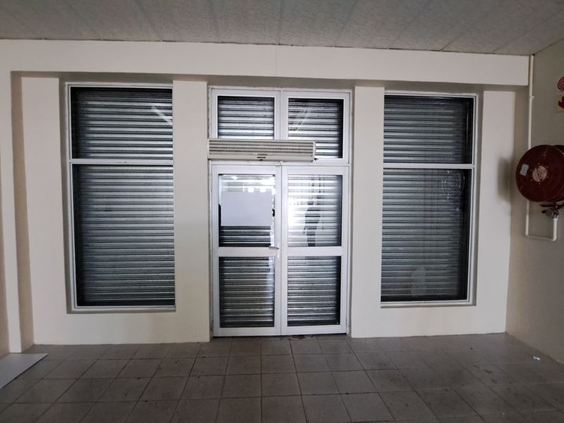 Retail entrance area featuring secure roller shutters, aluminium door frames, tiled flooring, and an integrated fire hose reel.
