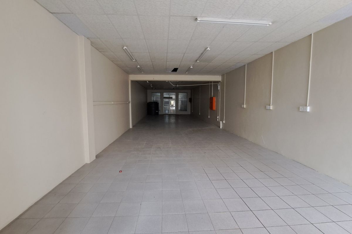 An empty, open-plan retail space featuring tiled flooring, a suspended ceiling with integrated lighting, and neutral wall finishes.