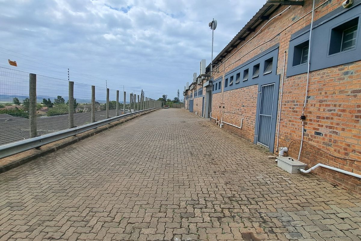 A paved exterior walkway along the rear of a brick retail building, featuring security fencing and external access points.