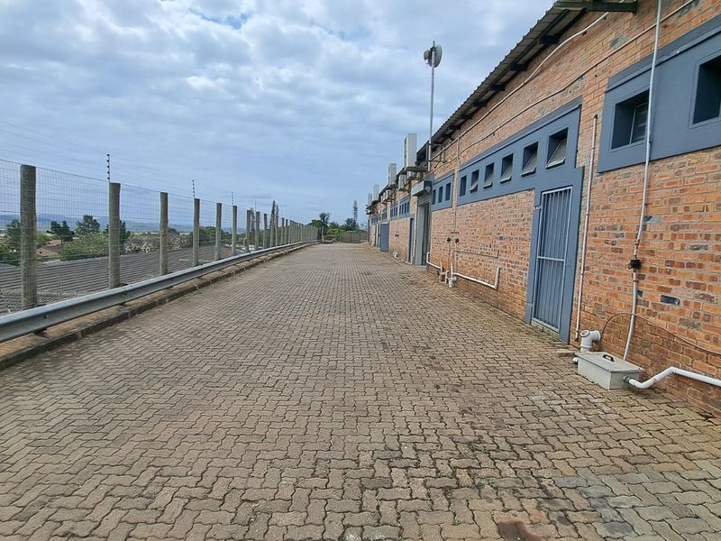 A paved exterior walkway along the rear of a brick retail building, featuring security fencing and external access points.