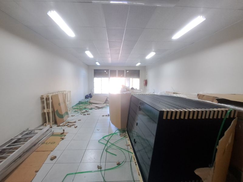 An open-plan retail space featuring tiled flooring, a suspended ceiling with integrated lighting, and a large window allowing natural light.