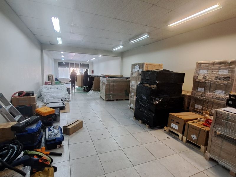 A functional retail utility or storage space featuring tiled flooring, suspended ceiling, and integrated fluorescent lighting, currently used for inventory storage.