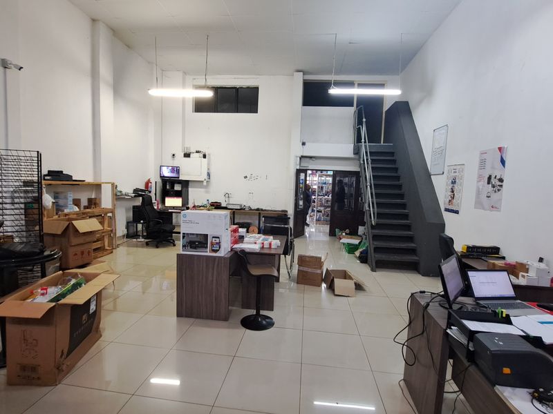 Open-plan commercial space featuring tiled flooring, a central staircase, and functional lighting, suitable for office or retail use.