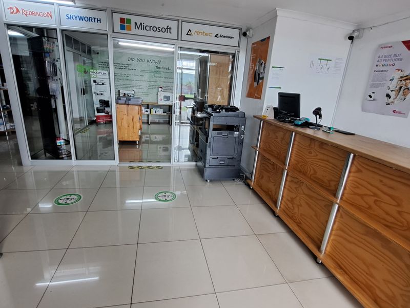 Commercial office entrance featuring a built-in wooden reception counter, tiled flooring, and glass partition walls leading to an inner office area.