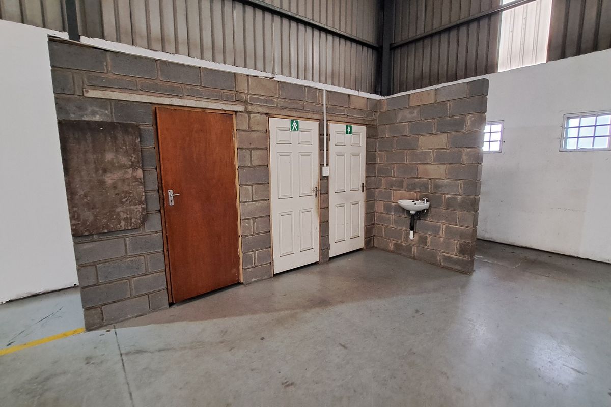 Industrial utility area featuring exposed concrete block walls, multiple access doors, a wall-mounted basin, and high-clearance steel roof structure.