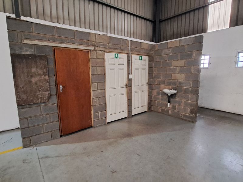 Industrial utility area featuring exposed concrete block walls, multiple access doors, a wall-mounted basin, and high-clearance steel roof structure.