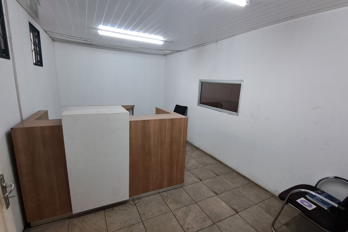 A functional office space featuring a built-in reception desk, tiled flooring, and fluorescent lighting, suitable for administrative or industrial reception use.