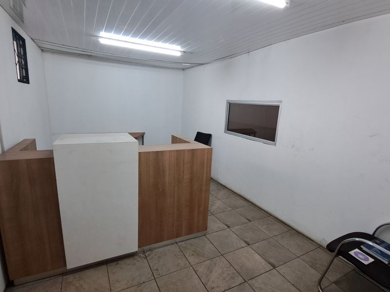 A functional office space featuring a built-in reception desk, tiled flooring, and fluorescent lighting, suitable for administrative or industrial reception use.