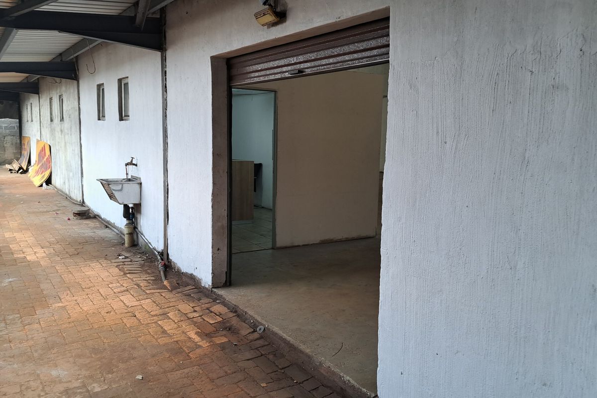 Rear exterior view of an industrial property featuring a paved walkway, external basin, and a roller shutter door entrance.