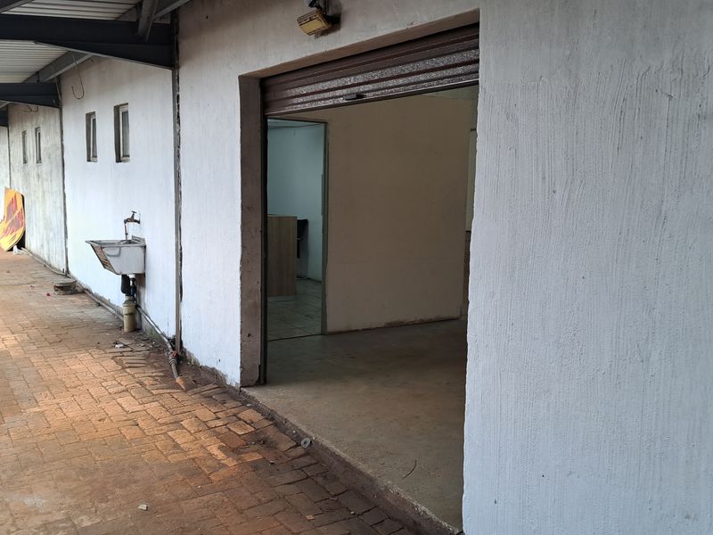 Rear exterior view of an industrial property featuring a paved walkway, external basin, and a roller shutter door entrance.