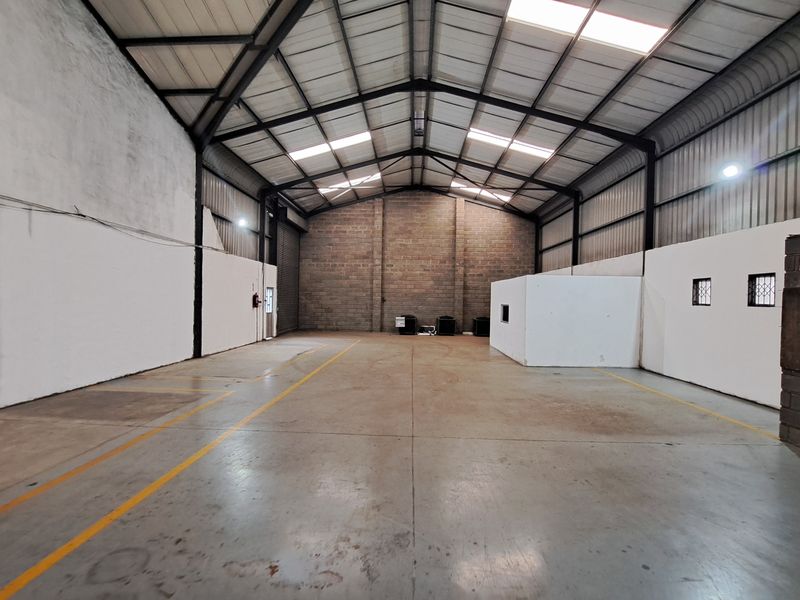 Spacious industrial warehouse unit featuring high ceilings with skylights, concrete flooring, and a large roller shutter door, suitable for storage or light manufacturing.