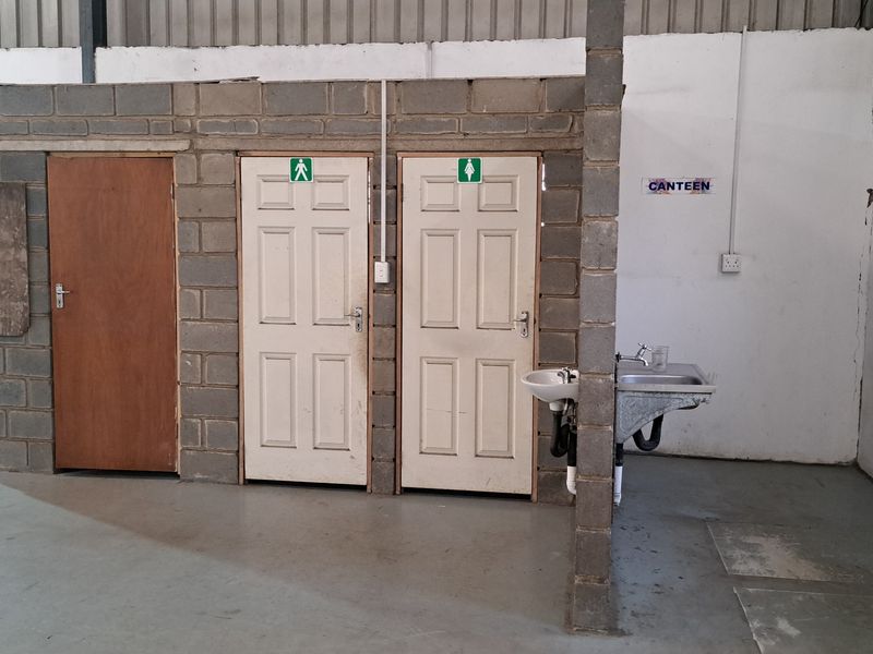 Industrial utility area featuring partitioned restroom access and a wall-mounted sink within a warehouse setting.