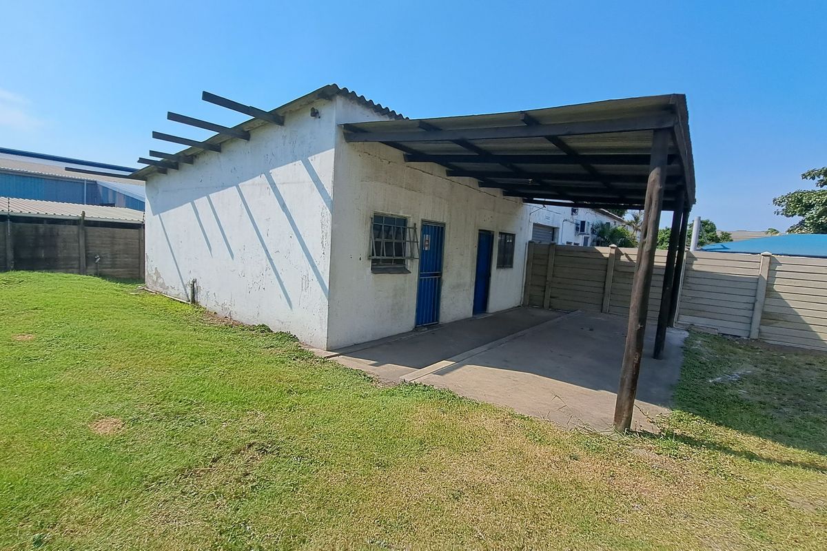 Rear view of an industrial outbuilding featuring a covered concrete patio area, security-barred windows, and perimeter precast concrete walling.