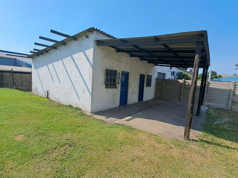 Rear view of an industrial outbuilding featuring a covered concrete patio area, security-barred windows, and perimeter precast concrete walling.