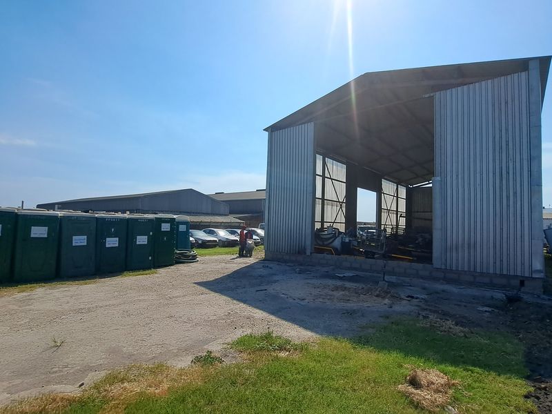 Industrial property featuring a large open-sided corrugated metal warehouse structure situated on a spacious, unpaved yard area.
