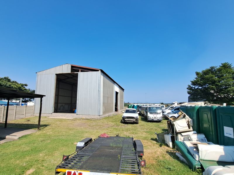 Rear exterior view of an industrial property featuring a large corrugated metal warehouse structure, open yard space, and perimeter walling.