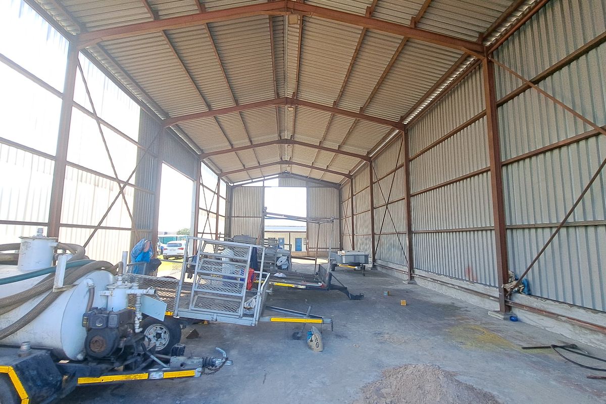 Spacious industrial warehouse or garage featuring a steel portal frame structure, corrugated metal walls, and a durable concrete floor.