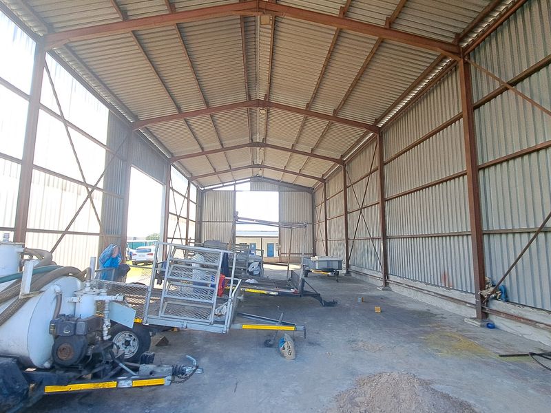 Spacious industrial warehouse or garage featuring a steel portal frame structure, corrugated metal walls, and a durable concrete floor.