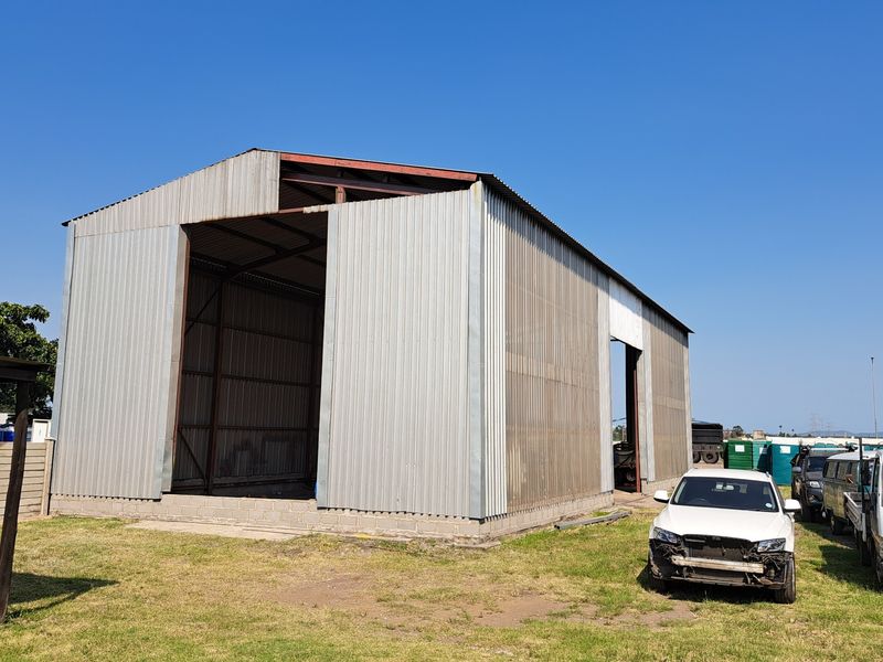 Industrial warehouse structure featuring a steel frame and corrugated metal cladding with large open bays, situated on a concrete block foundation.