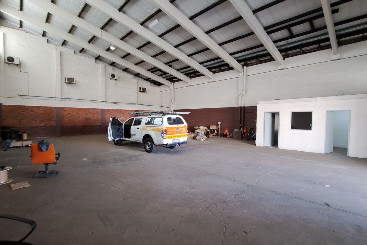 Spacious industrial warehouse unit featuring high ceilings with exposed steel trusses, concrete flooring, and integrated office space.