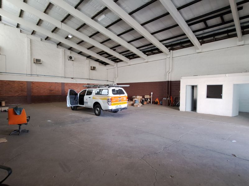 Spacious industrial warehouse unit featuring high ceilings with exposed steel trusses, concrete flooring, and integrated office space.