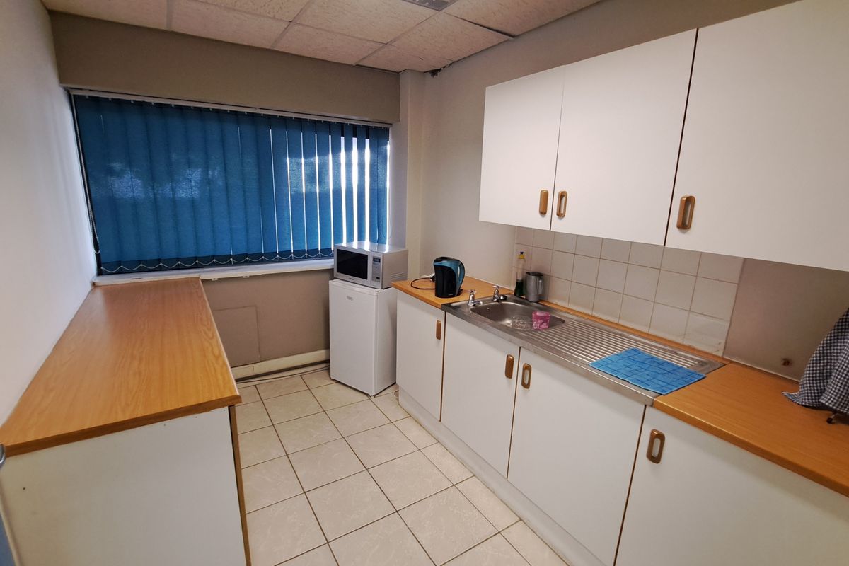 A functional office kitchenette featuring white cabinetry, laminate countertops, a stainless steel sink, and tiled flooring with a drop ceiling.