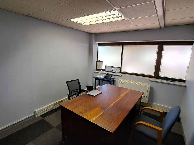A functional office space featuring carpet tiles, a suspended ceiling with recessed lighting, and frosted windows providing natural light.