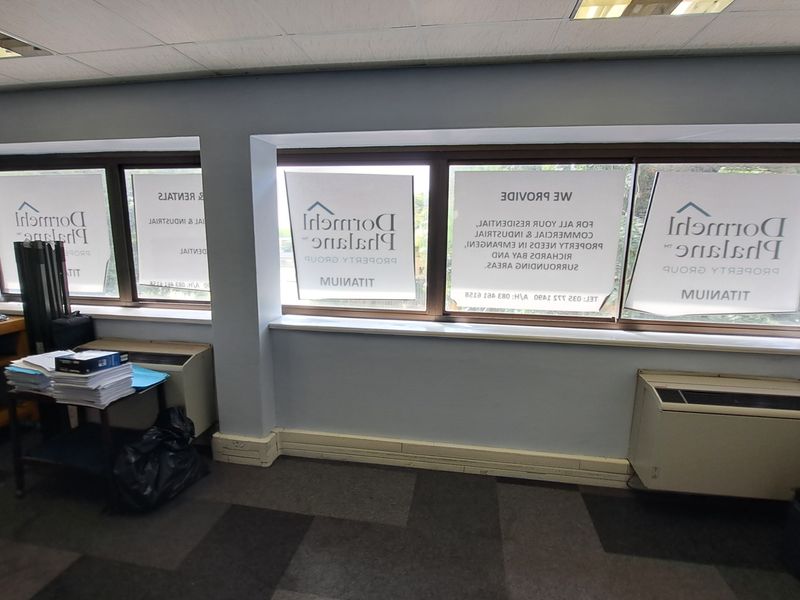 Office space featuring large windows with branding decals, suspended ceiling, recessed lighting, and carpeted flooring.