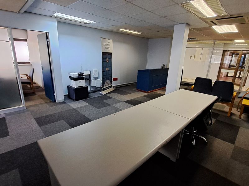 Open-plan office space featuring carpet tiles, suspended ceilings with recessed lighting, and glass partition walls creating a professional work environment.