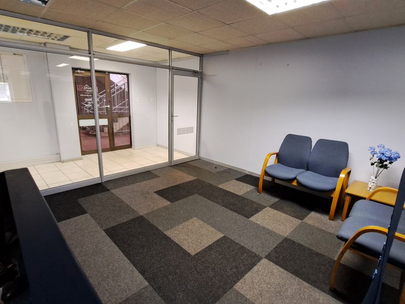 A professional office reception area featuring glass partitioning, carpet tile flooring, and a suspended ceiling with integrated lighting.
