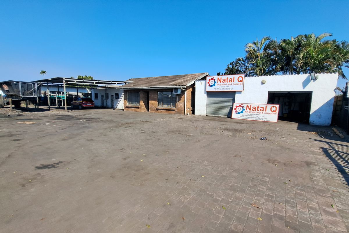 Industrial property featuring a large paved yard, covered parking area, and a brick and plaster building with roller shutter access.