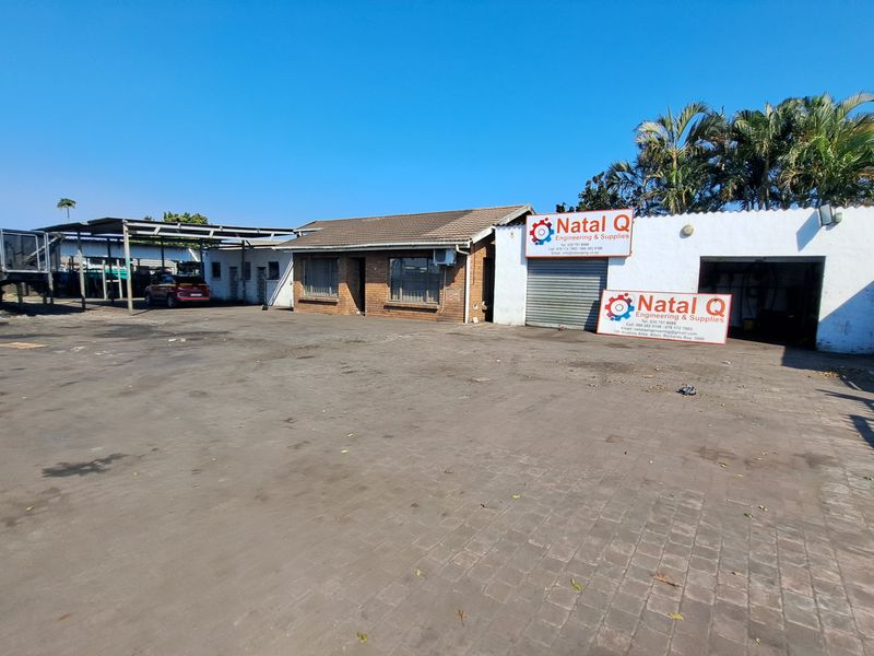 Industrial property featuring a large paved yard, covered parking area, and a brick and plaster building with roller shutter access.