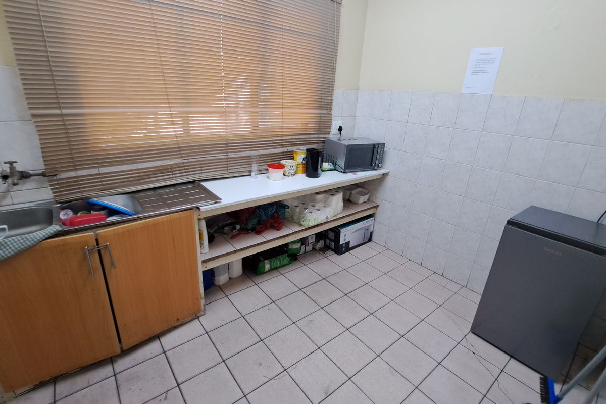 A functional industrial kitchen area featuring tiled flooring, a stainless steel sink, tiled splashbacks, and basic built-in cabinetry with open shelving.