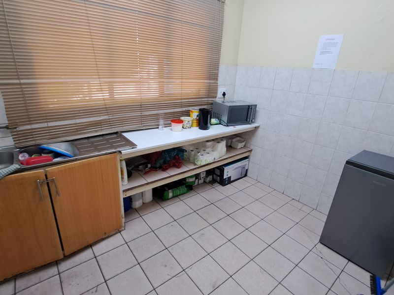 A functional industrial kitchen area featuring tiled flooring, a stainless steel sink, tiled splashbacks, and basic built-in cabinetry with open shelving.