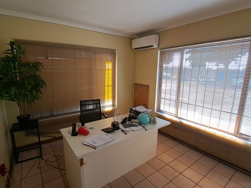 A functional office space featuring tiled flooring, split-system air conditioning, and large windows with fitted venetian blinds.