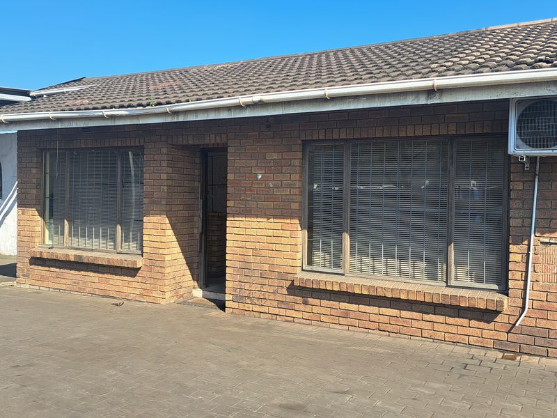 Front elevation of an industrial face brick building featuring a tiled roof, paved exterior area, and wall-mounted air conditioning unit.
