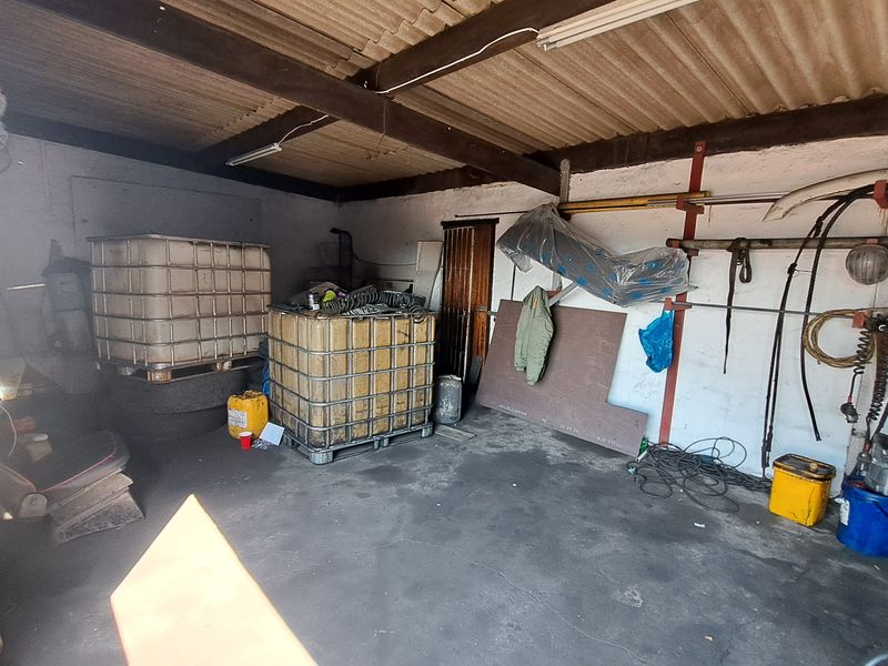 A functional industrial garage space featuring exposed timber beams, corrugated roofing, and concrete flooring, suitable for storage or workshop use.