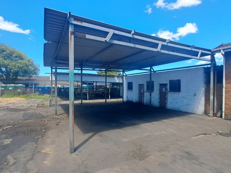 Industrial exterior area featuring a large metal carport structure, concrete paving, and access to adjacent brick and masonry building units.