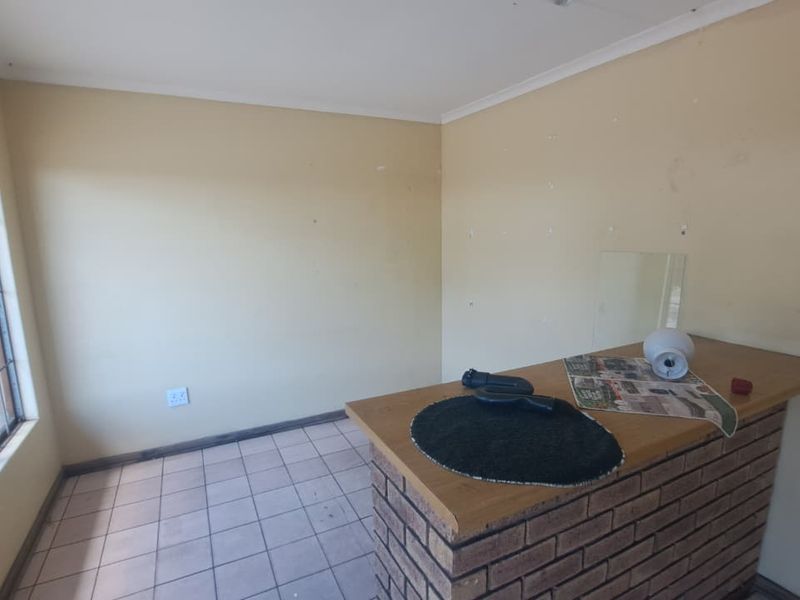A simple interior bar area featuring a brick counter, tiled flooring, and a window with security bars, offering potential for renovation.