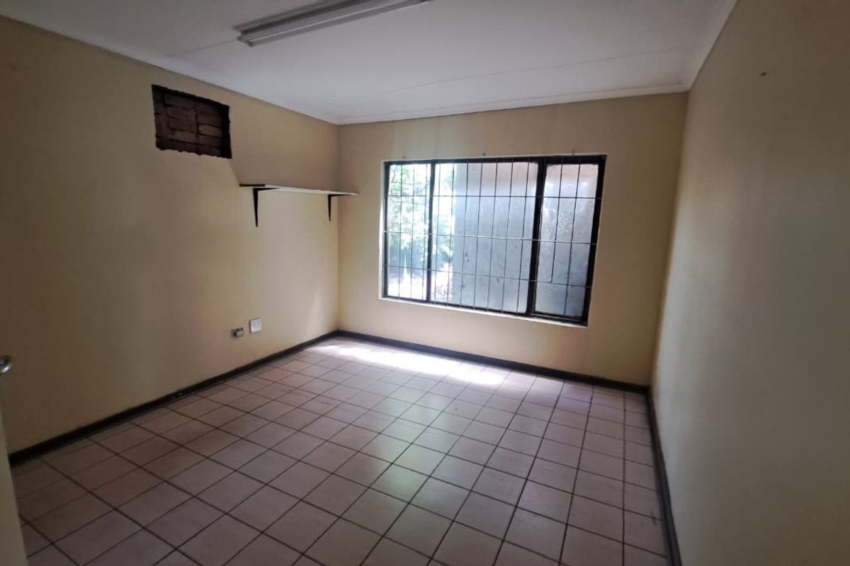 An empty bedroom featuring tiled flooring, a window with security bars, and a fluorescent light fixture, requiring minor wall repairs and cosmetic updates.