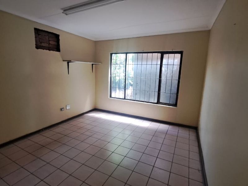 An empty bedroom featuring tiled flooring, a window with security bars, and a fluorescent light fixture, requiring minor wall repairs and cosmetic updates.