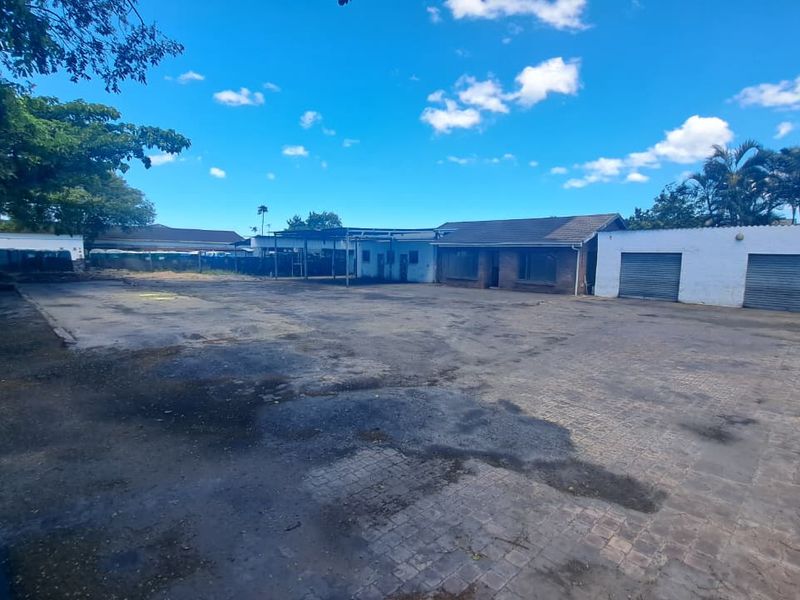 Industrial property exterior featuring a large paved yard, multiple roller shutter doors, and a covered parking area.